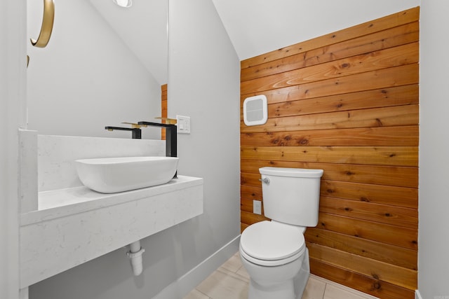 half bath featuring baseboards, lofted ceiling, a sink, tile patterned flooring, and toilet