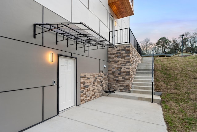 exterior entry at dusk with stucco siding, a patio, and a yard