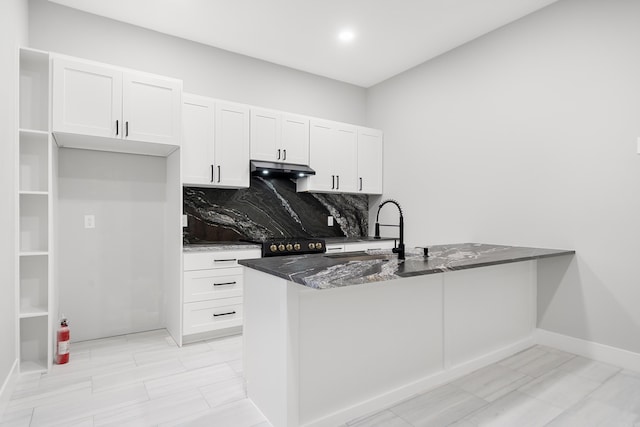 kitchen with under cabinet range hood, a sink, white cabinetry, dark stone counters, and a peninsula