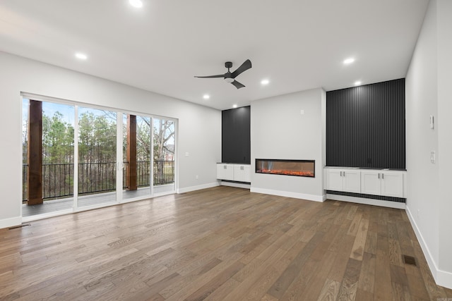 unfurnished living room with a glass covered fireplace, recessed lighting, wood finished floors, and visible vents