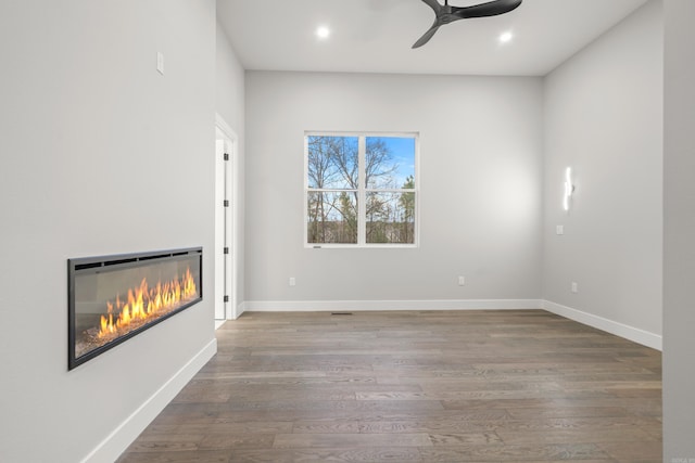 unfurnished living room with a glass covered fireplace, baseboards, wood finished floors, and recessed lighting