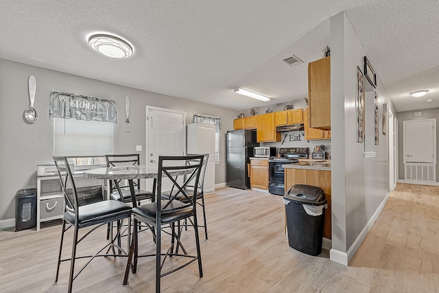 kitchen featuring visible vents, baseboards, under cabinet range hood, light wood-type flooring, and black appliances