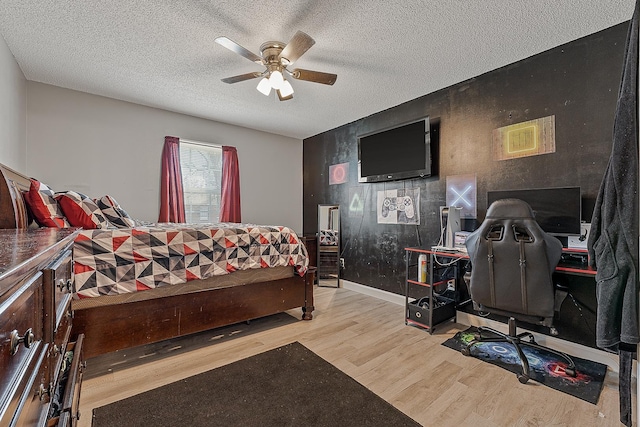 bedroom with a ceiling fan, a textured ceiling, wood finished floors, baseboards, and an accent wall