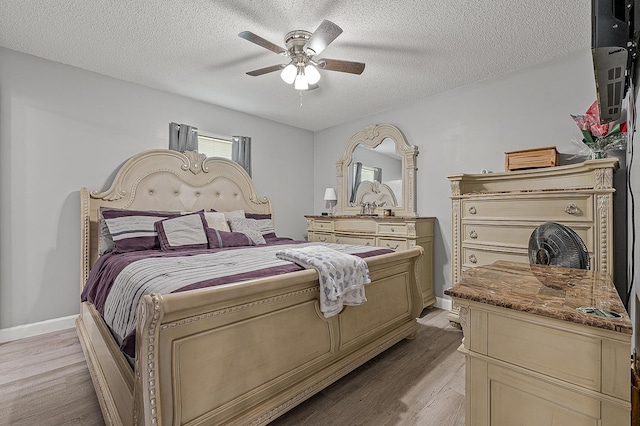 bedroom with ceiling fan, baseboards, a textured ceiling, and light wood-style flooring