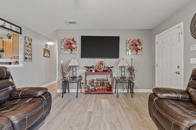 living room with visible vents, light wood-style flooring, a textured ceiling, and baseboards