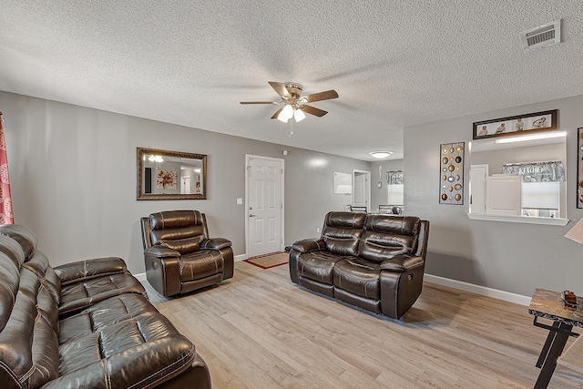 living area featuring wood finished floors, visible vents, baseboards, ceiling fan, and a textured ceiling