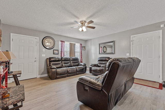 living room with a ceiling fan, light wood-type flooring, and a textured ceiling