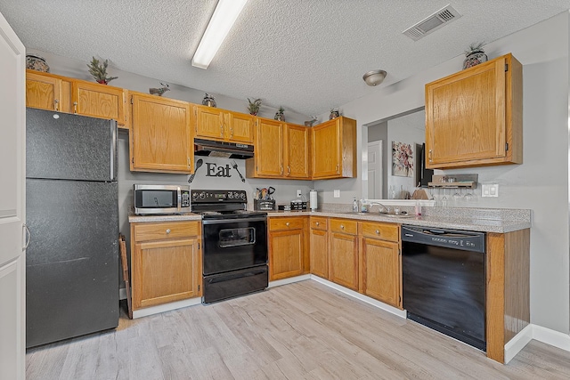 kitchen with light wood finished floors, visible vents, under cabinet range hood, light countertops, and black appliances