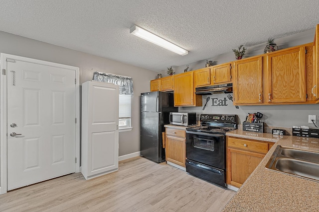 kitchen with under cabinet range hood, light wood-style flooring, black appliances, and a sink