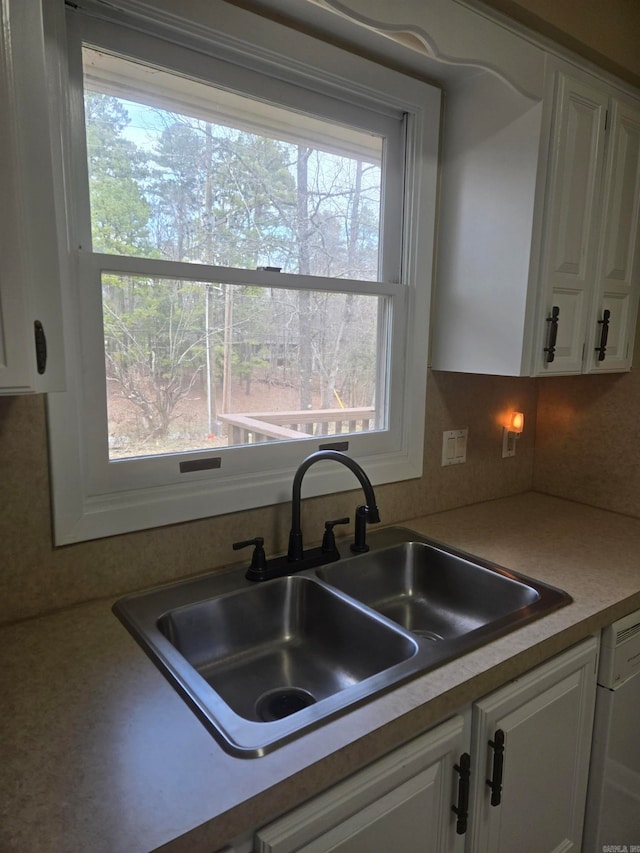 kitchen featuring dishwashing machine, white cabinets, light countertops, and a sink