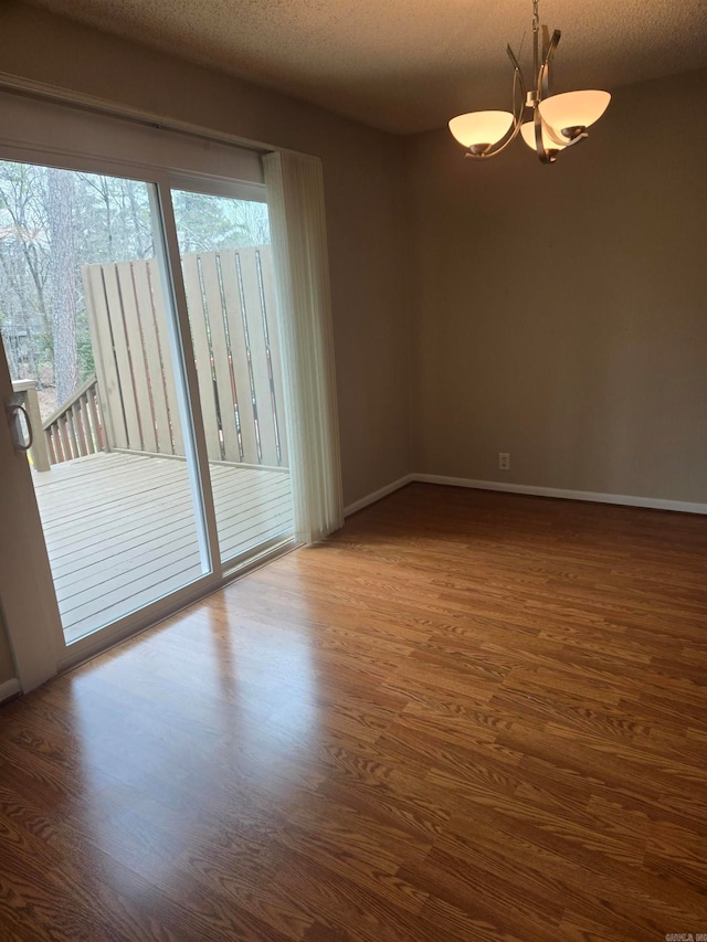 empty room featuring dark wood finished floors, an inviting chandelier, and a textured ceiling