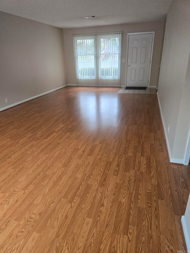 unfurnished room featuring a textured ceiling, baseboards, and wood finished floors