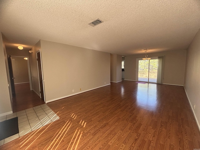 empty room with baseboards, wood finished floors, visible vents, and a textured ceiling