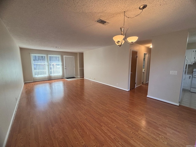 unfurnished living room featuring visible vents, baseboards, a textured ceiling, and wood finished floors