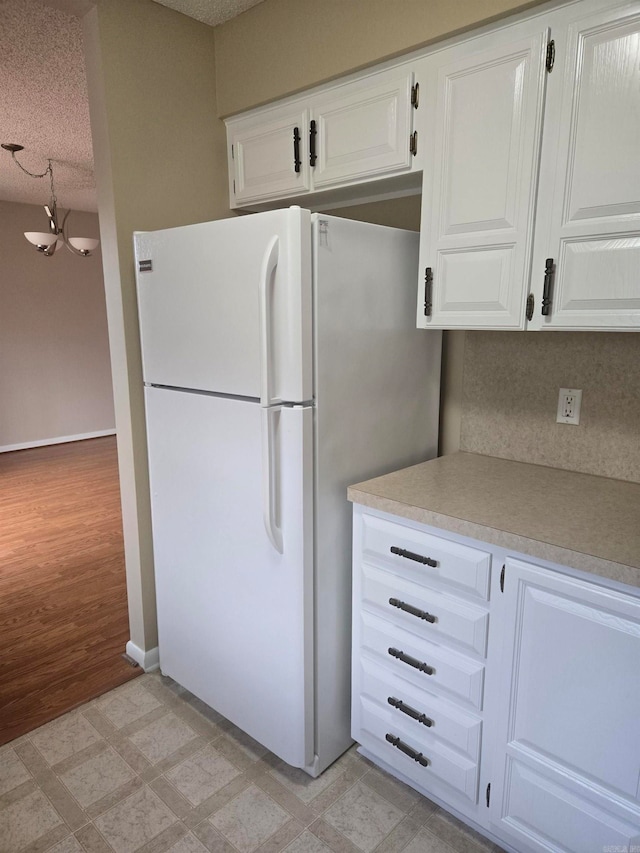 kitchen featuring light floors, freestanding refrigerator, light countertops, a textured ceiling, and white cabinetry