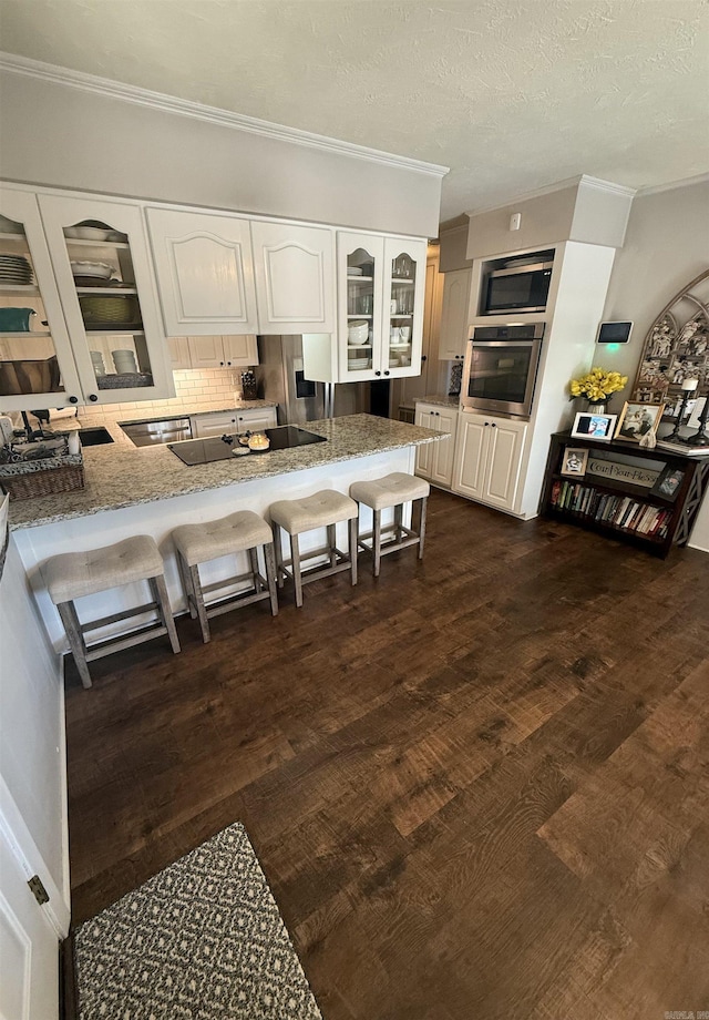 kitchen featuring a breakfast bar, stainless steel appliances, white cabinets, glass insert cabinets, and light stone countertops