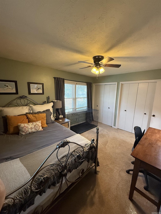 bedroom featuring light carpet, two closets, ceiling fan, and a textured ceiling