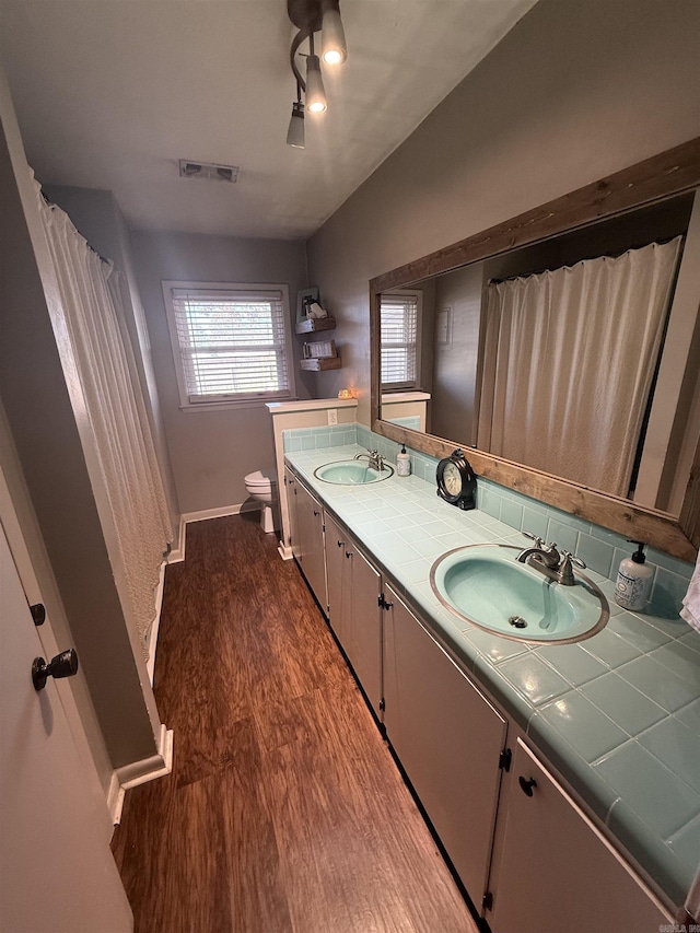 full bathroom featuring visible vents, toilet, double vanity, wood finished floors, and a sink