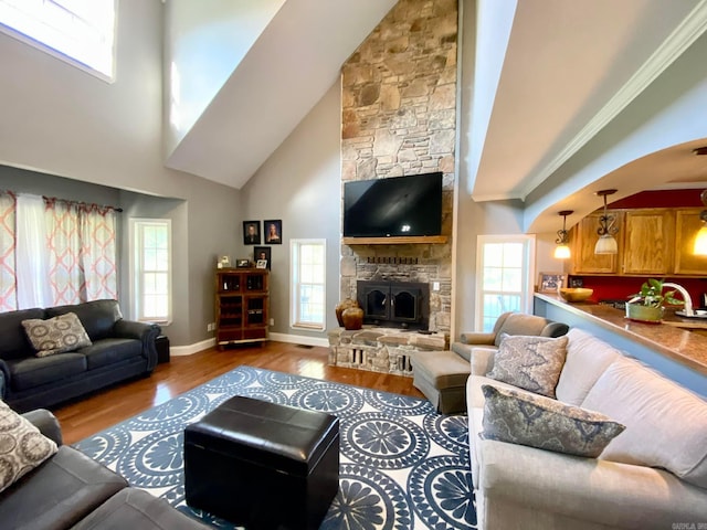 living room featuring a stone fireplace, crown molding, baseboards, and wood finished floors