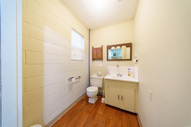 half bathroom featuring toilet, ornamental molding, a textured ceiling, wood finished floors, and vanity