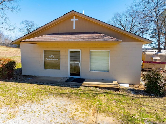 back of property with roof with shingles, concrete block siding, a lawn, and a patio area