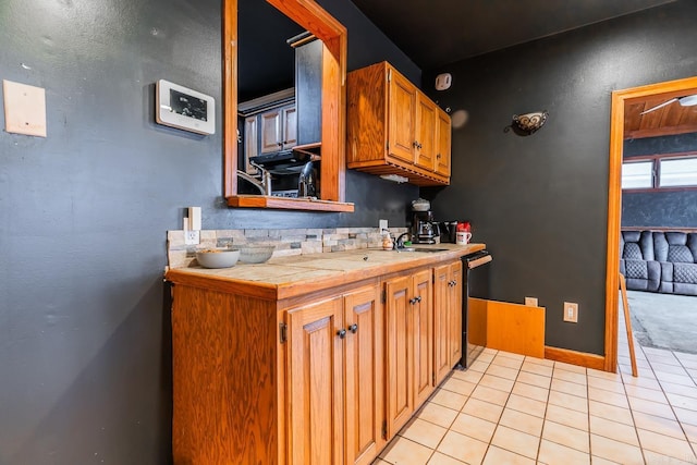 kitchen featuring dishwashing machine, light tile patterned floors, a sink, tile counters, and brown cabinets