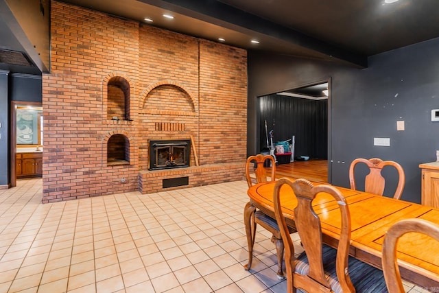 dining room with light tile patterned floors, beamed ceiling, brick wall, and a fireplace