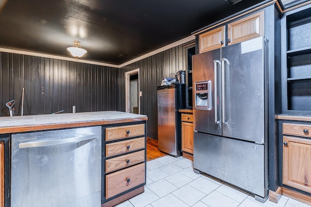 kitchen with light tile patterned floors, wooden walls, appliances with stainless steel finishes, and ornamental molding