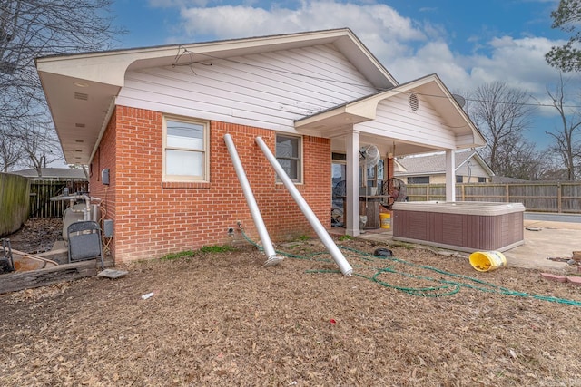 rear view of property featuring brick siding, cooling unit, a hot tub, and a fenced backyard