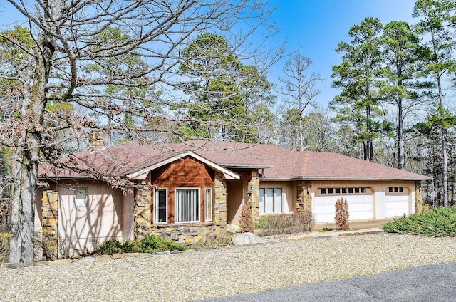 view of front of property featuring an attached garage, stone siding, and roof with shingles