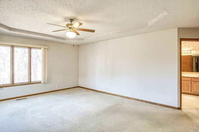 spare room featuring visible vents, baseboards, light colored carpet, a textured ceiling, and a ceiling fan