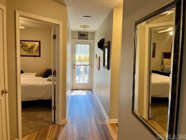 hallway featuring visible vents, baseboards, a textured ceiling, and wood finished floors