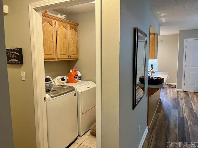 clothes washing area with washing machine and clothes dryer, cabinet space, light wood-type flooring, and baseboards