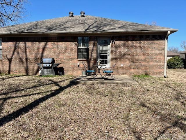 rear view of property with a patio area, brick siding, a lawn, and a shingled roof