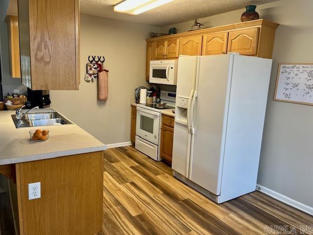 kitchen with a sink, wood finished floors, white appliances, light countertops, and baseboards