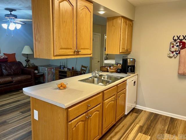 kitchen featuring a ceiling fan, baseboards, dark wood-style flooring, a sink, and light countertops