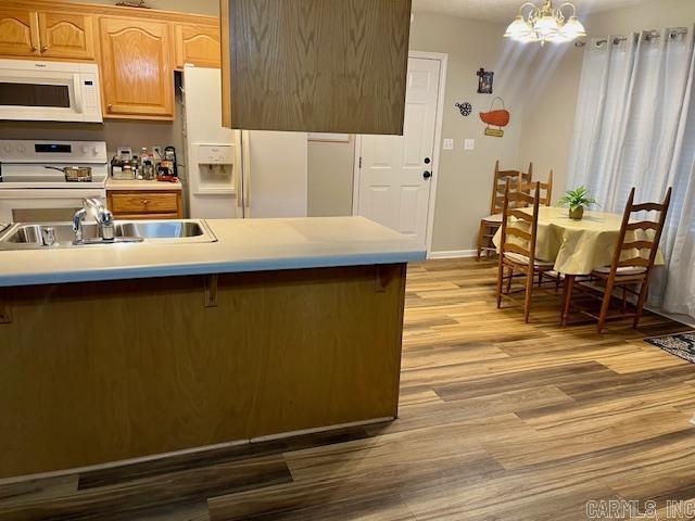 kitchen with light countertops, light wood-style floors, a notable chandelier, white appliances, and a sink