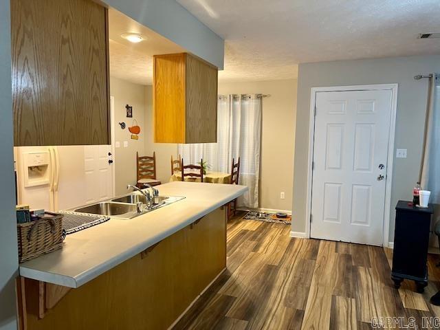 kitchen featuring visible vents, baseboards, dark wood finished floors, brown cabinetry, and a sink