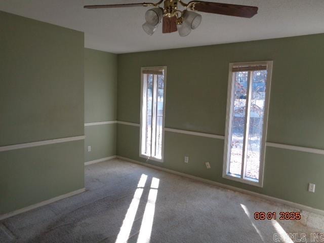 carpeted spare room with plenty of natural light, a ceiling fan, and baseboards