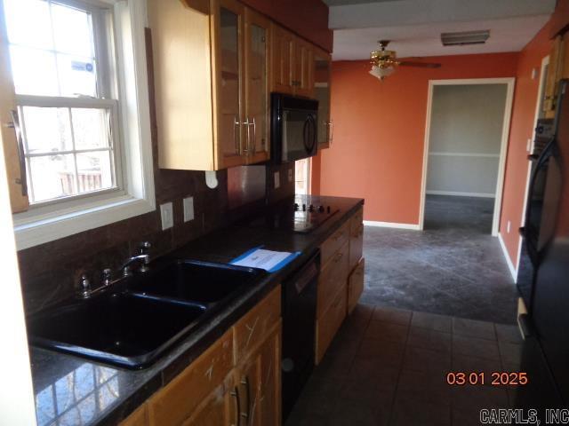 kitchen featuring brown cabinetry, a sink, decorative backsplash, black appliances, and dark countertops