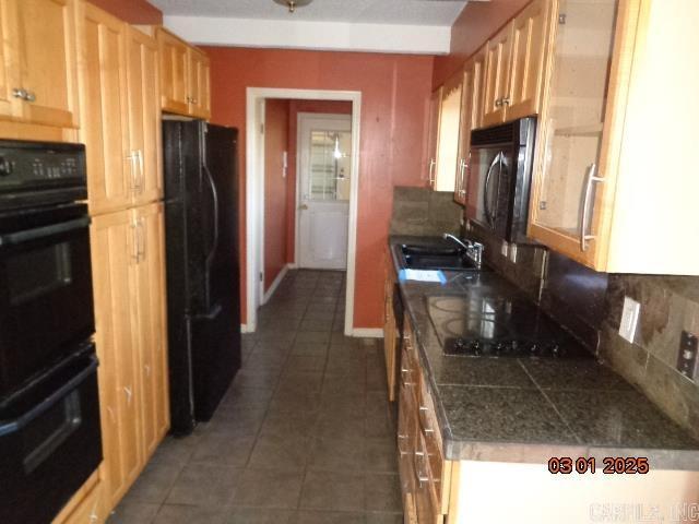 kitchen featuring tasteful backsplash, dark tile patterned flooring, tile countertops, black appliances, and a sink