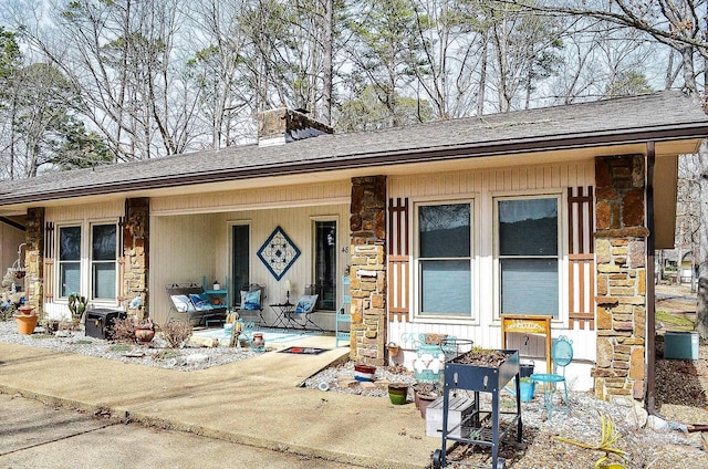 doorway to property featuring stone siding, a porch, a chimney, and roof with shingles