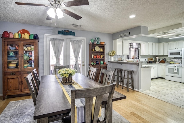 dining space featuring ceiling fan, light wood-style flooring, visible vents, and a textured ceiling