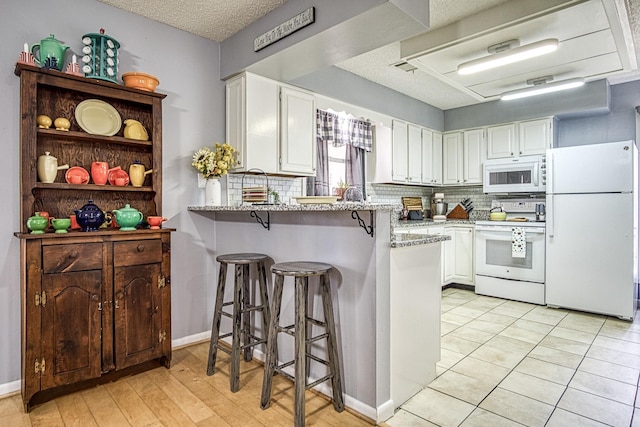 kitchen featuring light stone counters, white cabinets, white appliances, and a kitchen breakfast bar