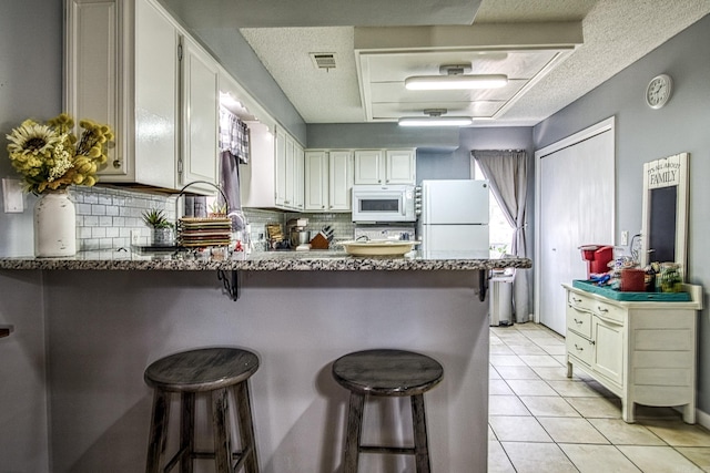 kitchen featuring white appliances, light tile patterned floors, visible vents, a peninsula, and tasteful backsplash