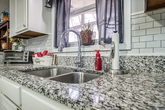 kitchen with white cabinets, light stone counters, tasteful backsplash, and a sink