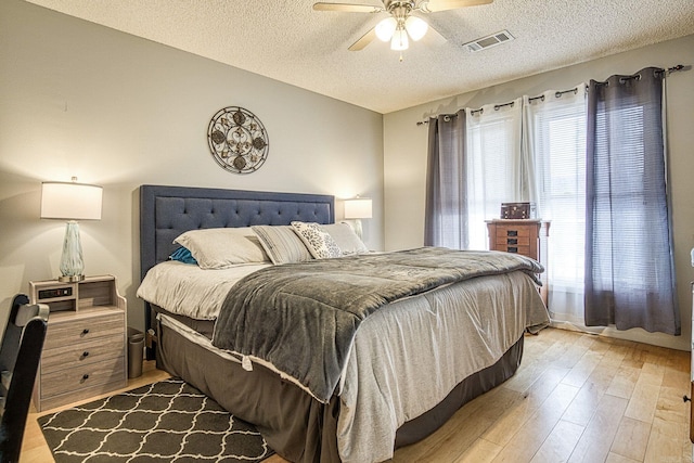 bedroom with visible vents, light wood-style flooring, a textured ceiling, and ceiling fan