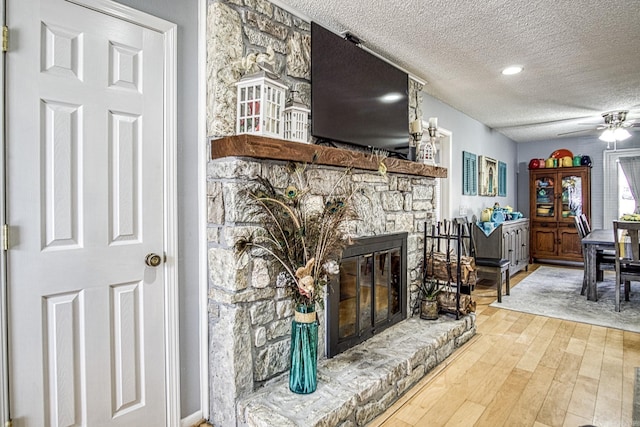 living room with a ceiling fan, wood finished floors, a fireplace, and a textured ceiling