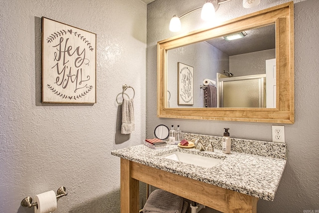 bathroom with an enclosed shower, a textured wall, and a sink