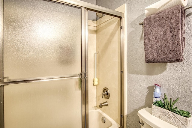 bathroom with toilet, a textured wall, and enclosed tub / shower combo